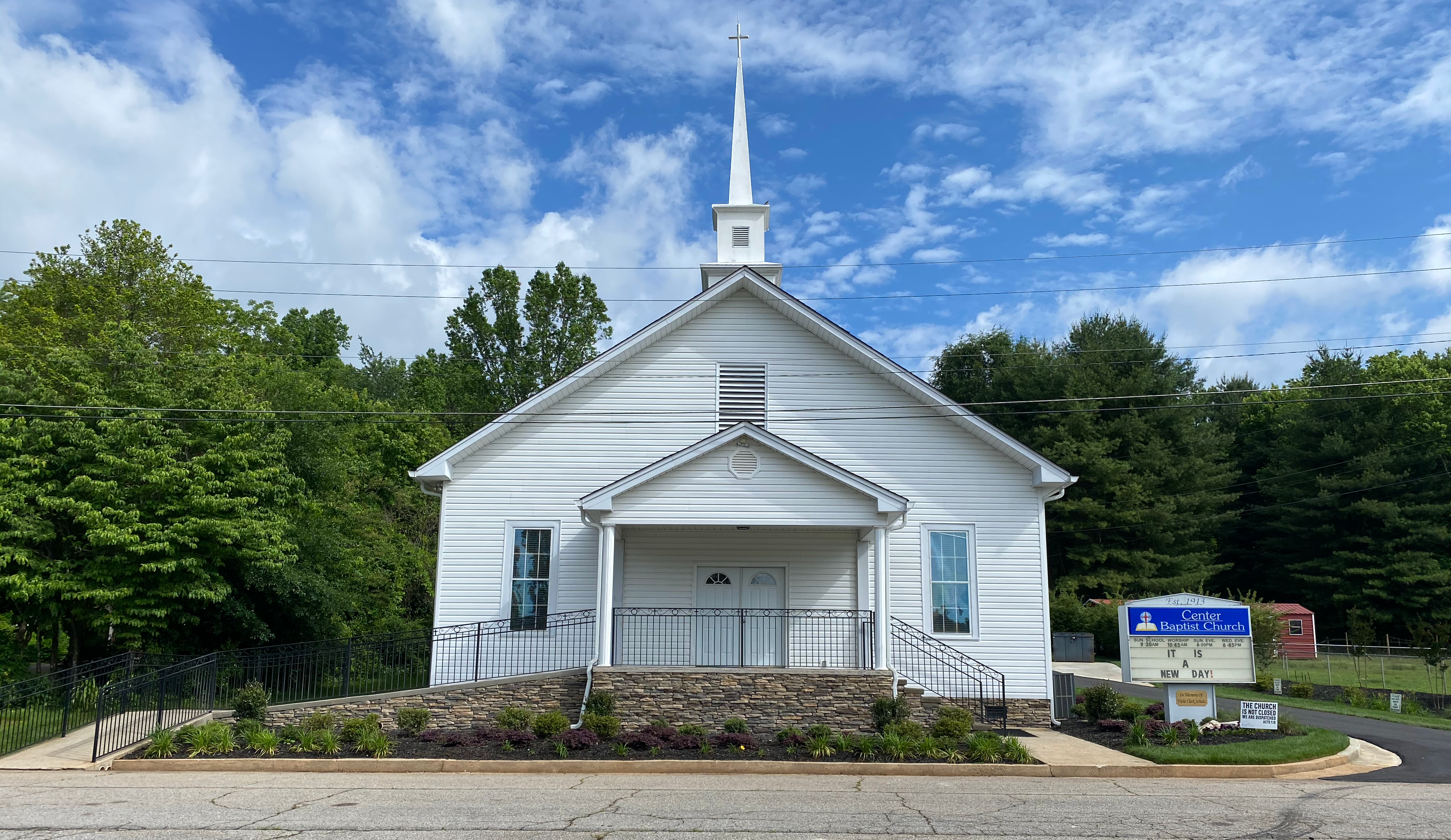 Church Building sits between a tree line and parking lot with bright sky overhead.